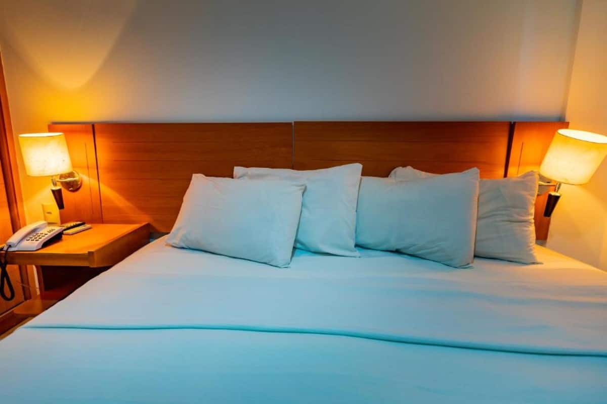 A hotel room with a large bed, two bedside lamps, a bedside phone, and a wooden headboard.