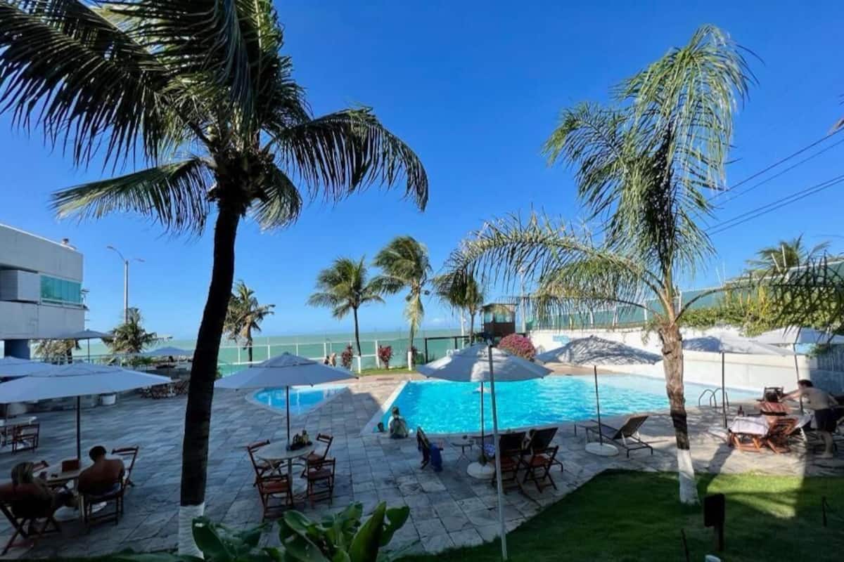 A pool area with lounge chairs, umbrellas, and palm trees.