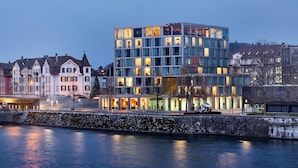A modern hotel with multiple floors, large windows, and a view of the river. - H4 Hotel Solothurn (Solothurn)