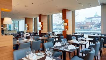 A modern restaurant with multiple dining tables, chairs, and large windows offering a view of a historic building.