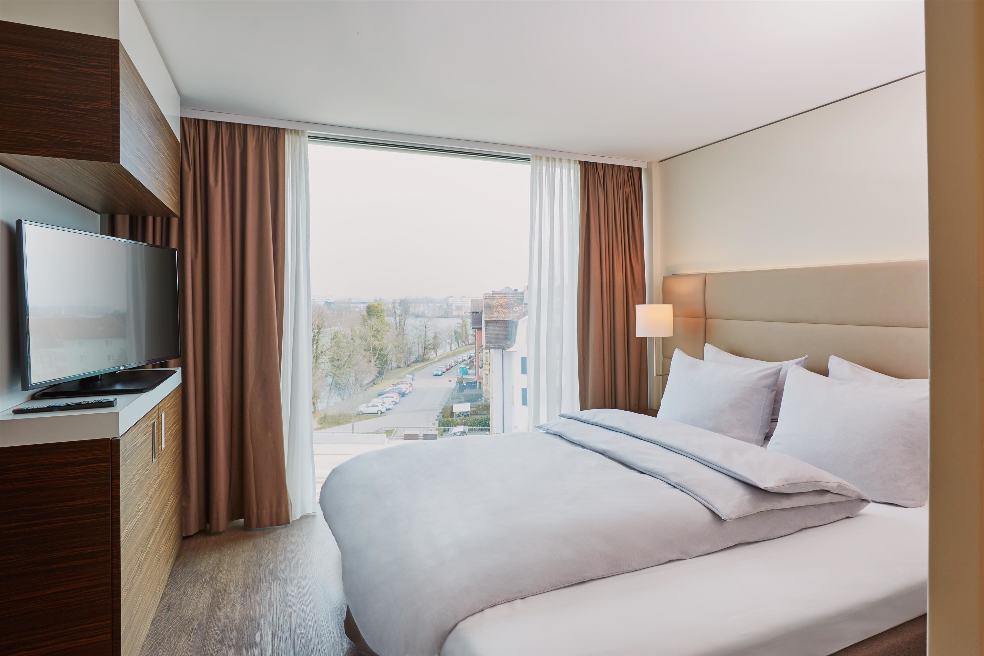 Une chambre d’hôtel avec un grand lit, un téléviseur à écran plat, une armoire en bois et une vue sur la ville par la fenêtre.