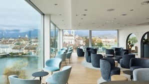 A modern lounge area with seating and a large window offering a view of a cityscape and river. - H4 Hotel Solothurn (Solothurn)