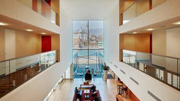 A spacious lobby with a high ceiling, a central seating area, and a large window overlooking a scenic view.