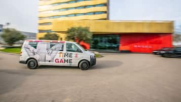 A white van with "TIME FOR A GAME" and "GRAND CASINO BASEL" on the side, parked in front of a modern building with a red facade and yellow windows.