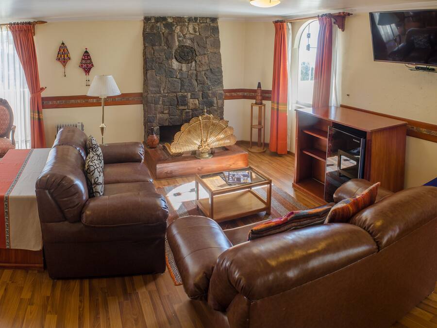 A living room with a stone fireplace, leather sofas, a coffee table, and a flat-screen TV mounted on the wall.