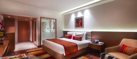 Habitación de hotel con cama, sillón de masajes, escritorio con computadora y mesita de noche con teléfono.