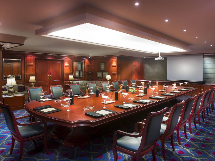 A conference room with a long table, chairs, and a projector screen.