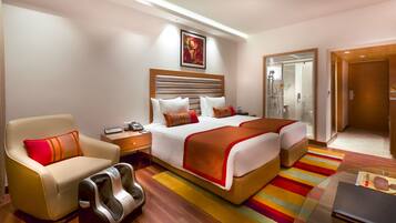A hotel room with a bed, a massage chair, a bedside table with a phone, a shower area, and a door leading to another room.