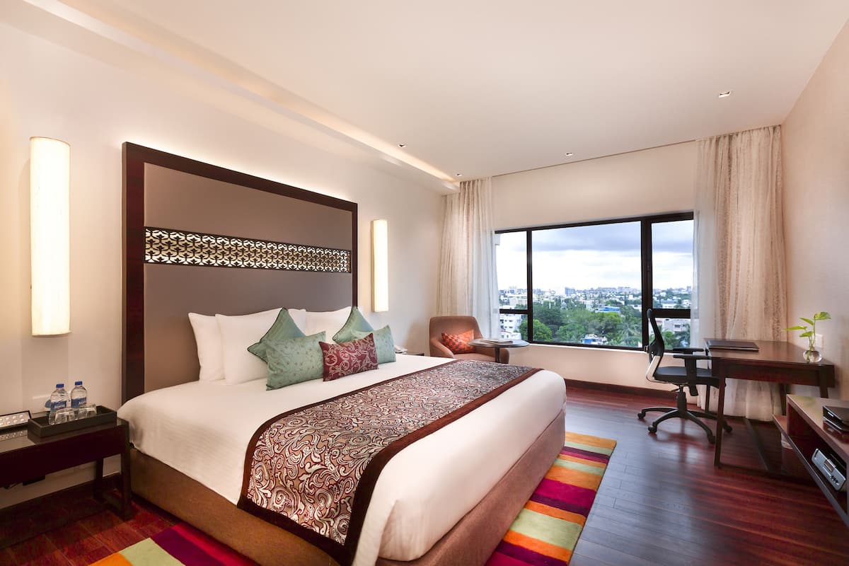 Ein Hotelzimmer mit einem großen Bett, einem Schreibtisch, einem Sessel und Blick auf die Stadt.