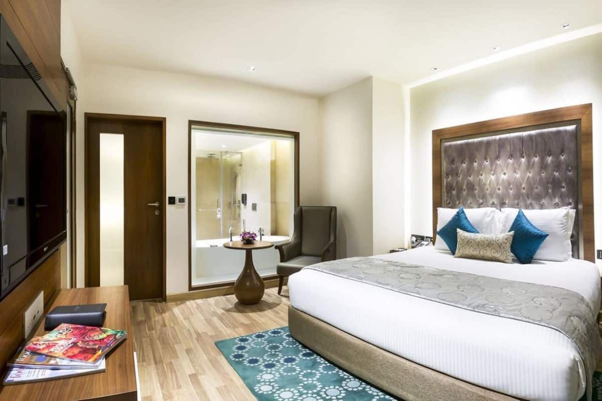 Ein Hotelzimmer mit einem großen Bett, einem Schreibtisch mit einer Zeitschrift, einem Spiegel und einer Duschkabine.