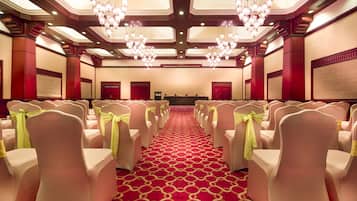 A hotel conference room with rows of chairs, a red carpet, and chandeliers.