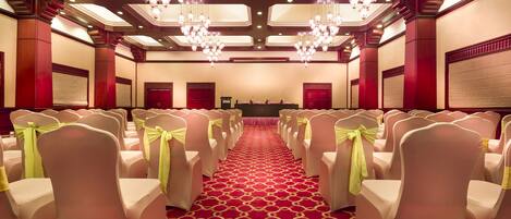 A hotel conference room with rows of chairs, a red carpet, and chandeliers.