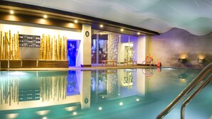 An indoor swimming pool with clear water, wooden deck, and a stone wall. - Grand Chennai by GRT Hotels (Chennai)