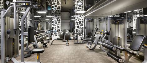 Une salle de sport équipée de divers appareils d’exercice, notamment des machines de musculation, des poids libres et un grand ballon d’exercice.