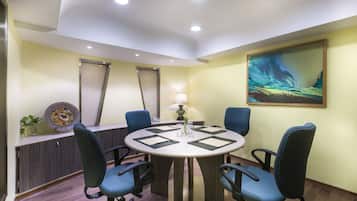 A conference room with a round table, four chairs, a lamp, and a painting on the wall.