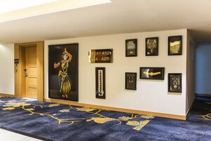 Een gang met een tapijtvloer, een deur met het nummer 425, en verschillende lijstwerken aan de muur.