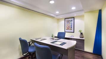 A conference room with a long table, two blue chairs, a small plant, and a framed artwork on the wall.