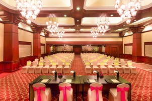 A conference room with rows of chairs, tables with nameplates, and chandeliers.