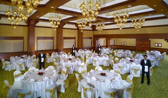 A banquet hall with round tables, white tablecloths, and gold sashes on chairs.
