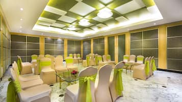 Un salón de conferencias con filas de sillas color beige, cada una con un lazo verde, y una mesa de vidrio en el centro.