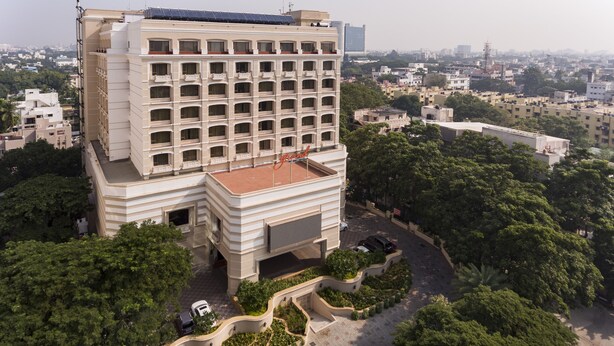 A multi-story hotel with a rooftop terrace, surrounded by greenery and other buildings. - Grand Chennai by GRT Hotels (Chennai)