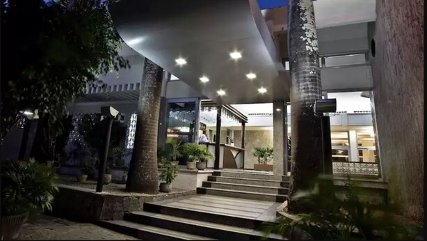 A modern building with a covered entrance, steps leading up to it, and potted plants around. - Arituba Park Hotel (Natal)