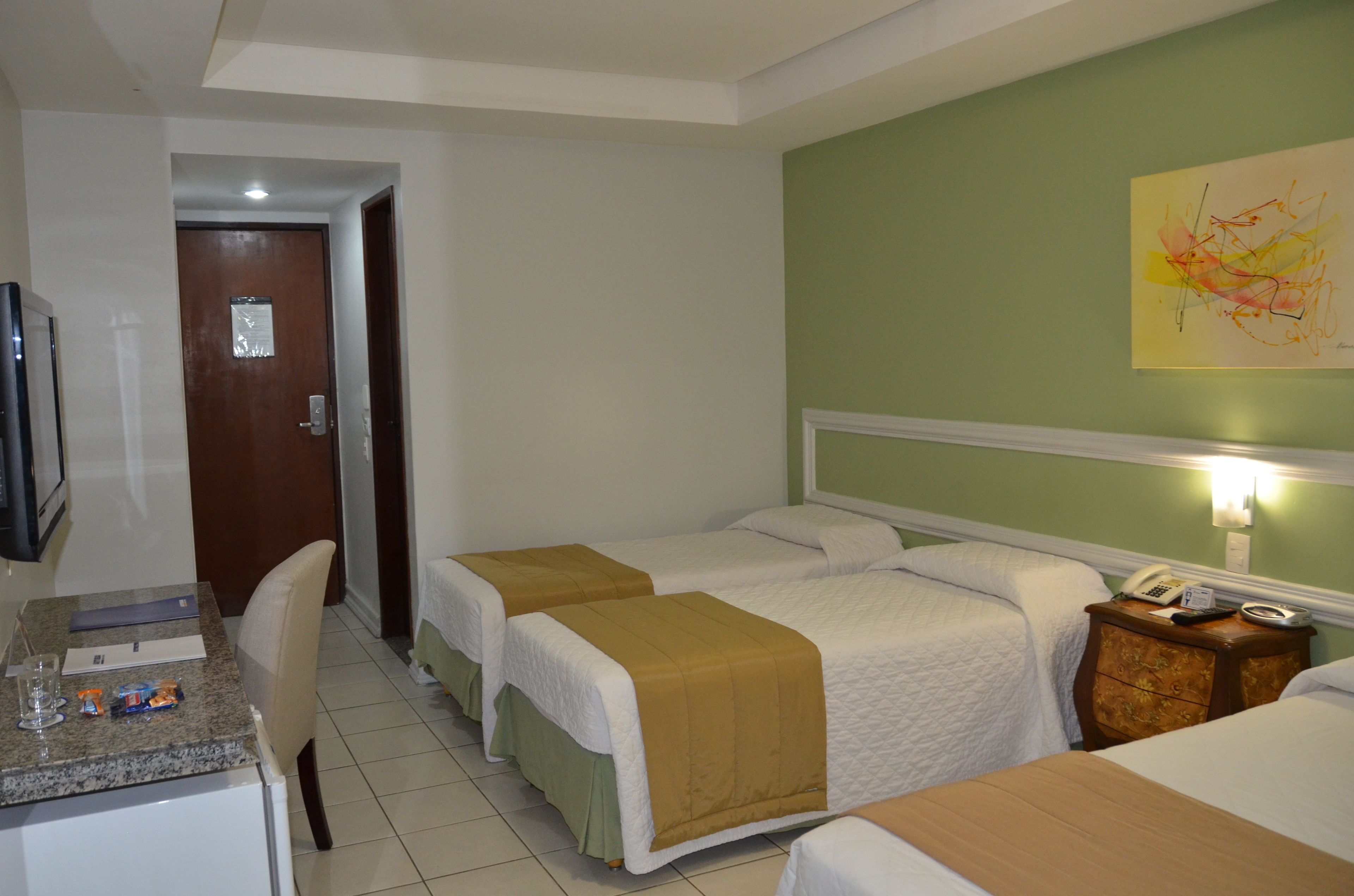 A hotel room with two beds, a desk with a chair, a television, and a wall-mounted phone.