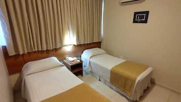 Ein Hotelzimmer mit zwei Einzelbetten, einem Nachttisch, einem Telefon und einem Fenster mit Vorhängen.