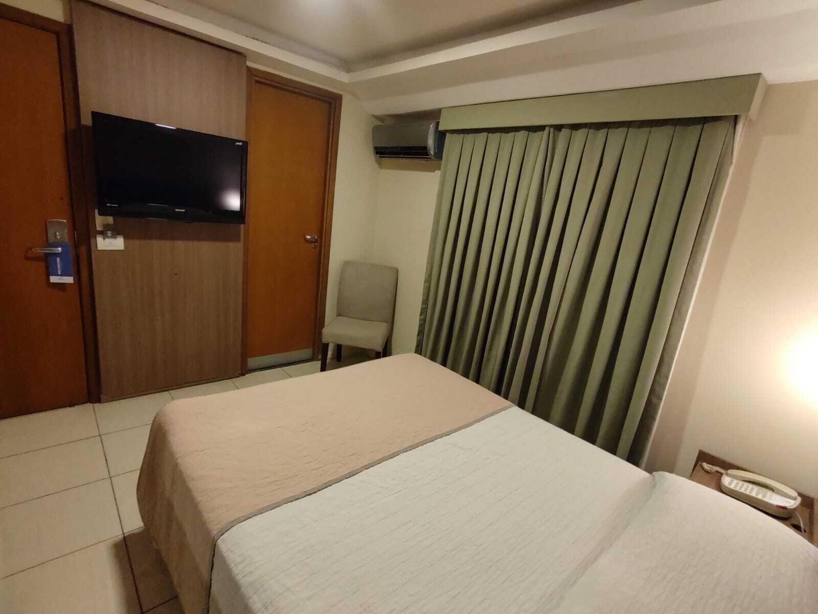 Una habitación de hotel con cama, una silla, televisión, aire acondicionado y teléfono.