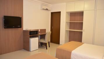 Habitación de hotel con dos camas, un televisor, un escritorio con ordenador, una silla y un armario.
