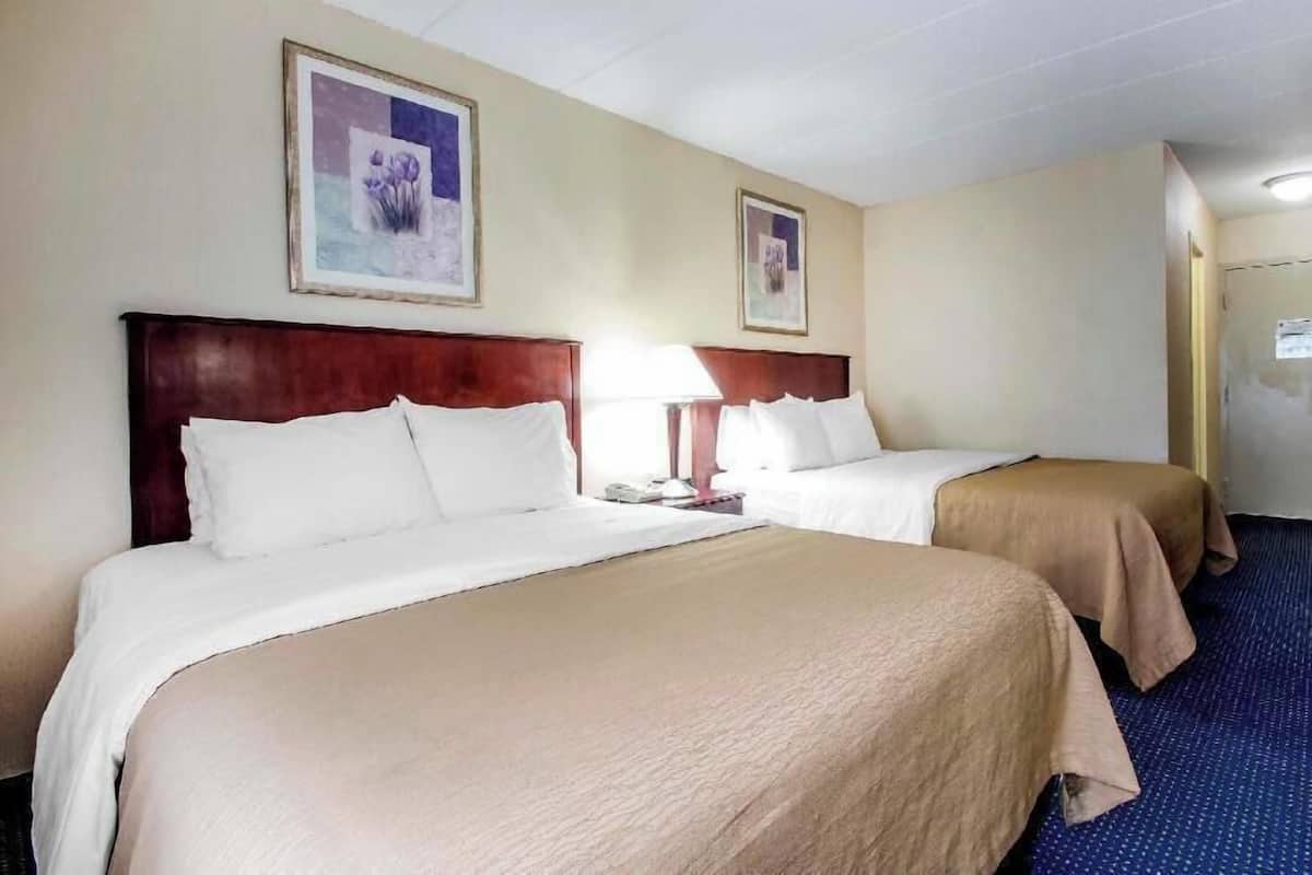 A hotel room with two beds, a wooden headboard, a nightstand, and a lamp.