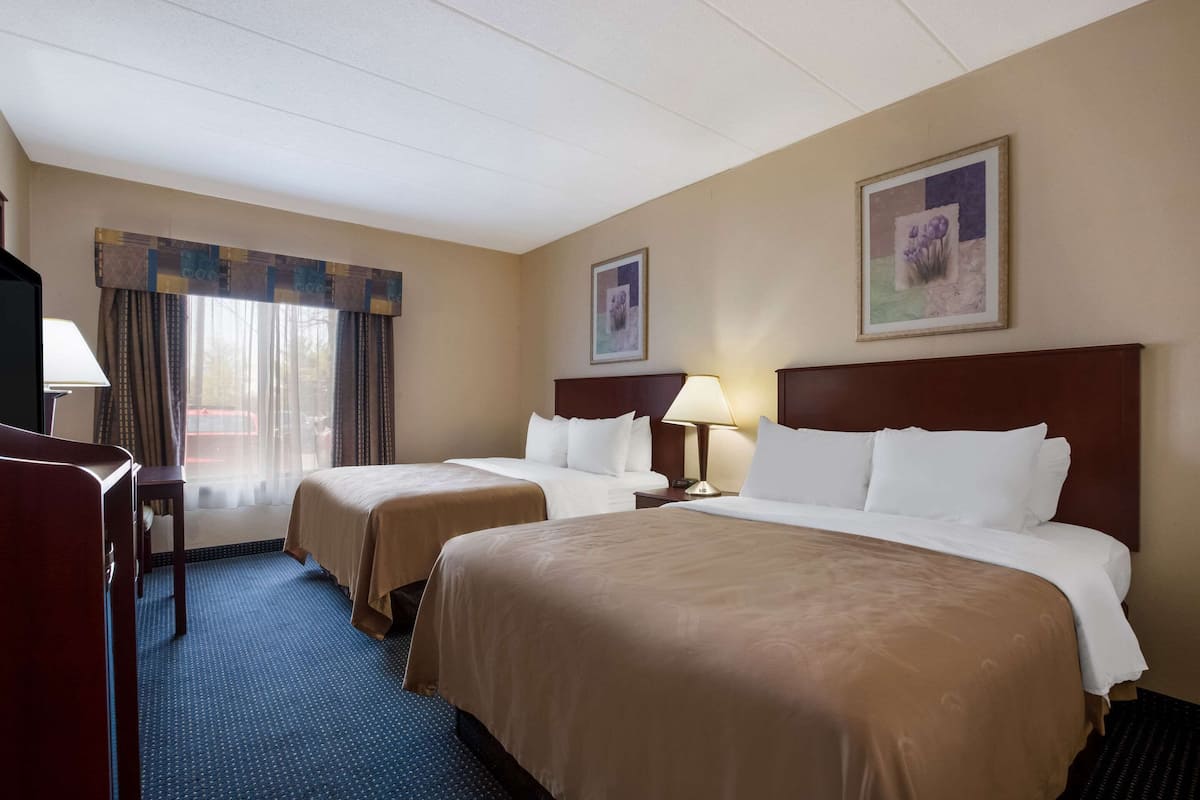 A hotel room with two beds, a desk, and a chair.