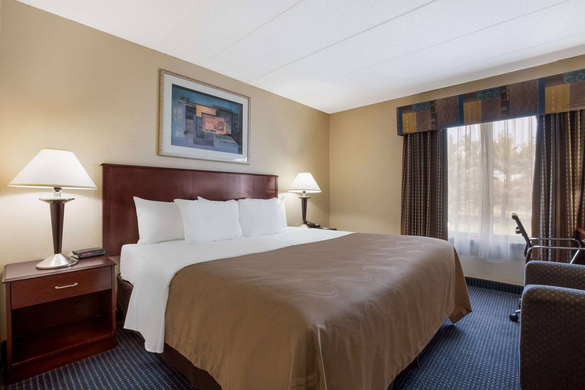 A hotel room with a large bed, two bedside tables with lamps, a framed picture on the wall, and a window with curtains.