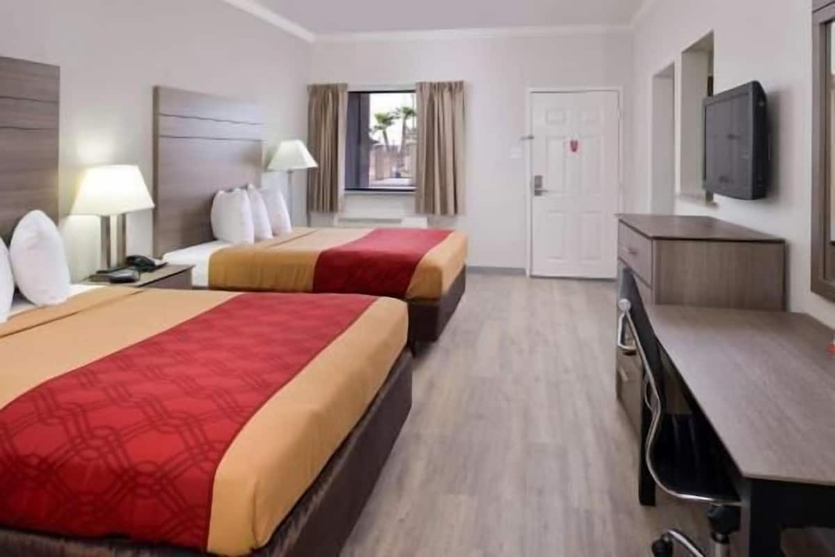 A hotel room with two beds, a desk, a TV, and a window with curtains.