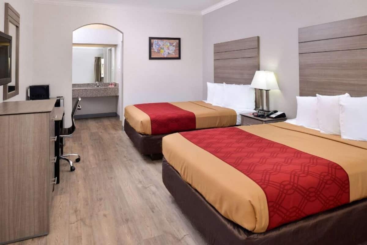 A hotel room with two beds, a desk, a mirror, and a television.