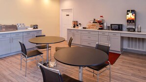 A modern kitchen with two round tables, chairs, a microwave, a coffee machine, and various appliances. - Econo Lodge Inn & Suites Port Arthur near Sabine Pass (Port Arthur)