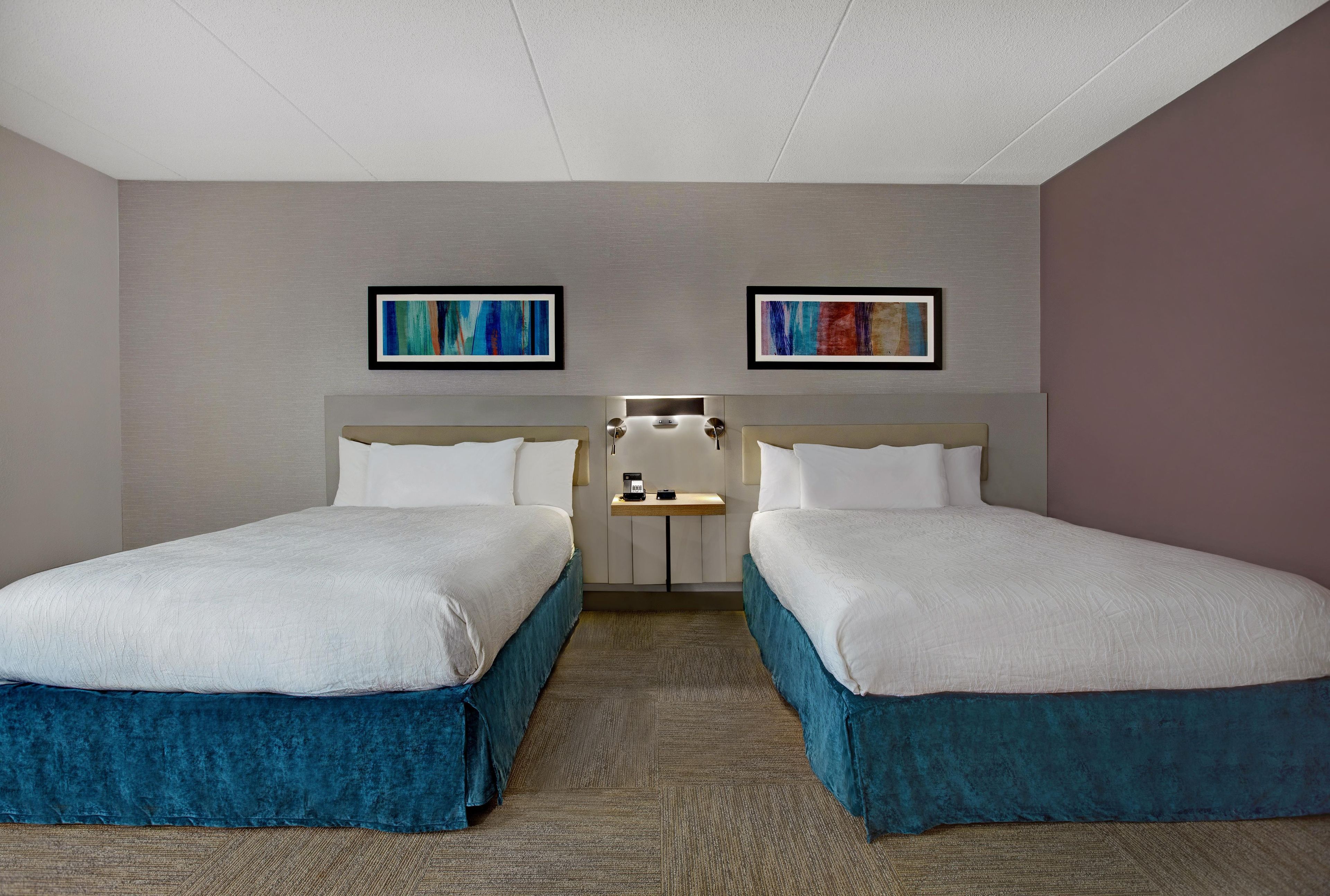 A hotel room with two beds, a small table with a phone, and artwork on the walls.