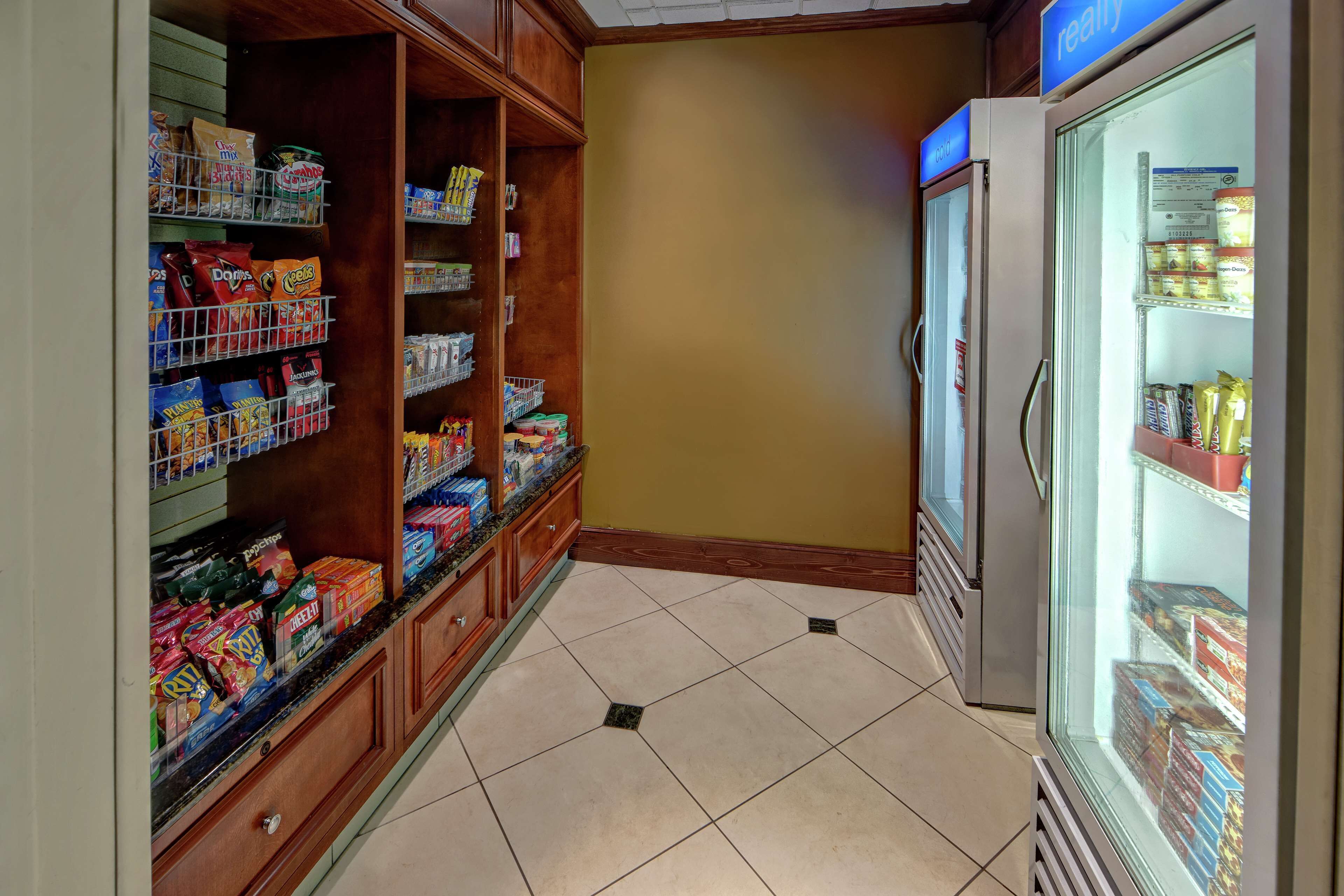 A grocery store with shelves stocked with snacks and beverages, a freezer, and a tiled floor.