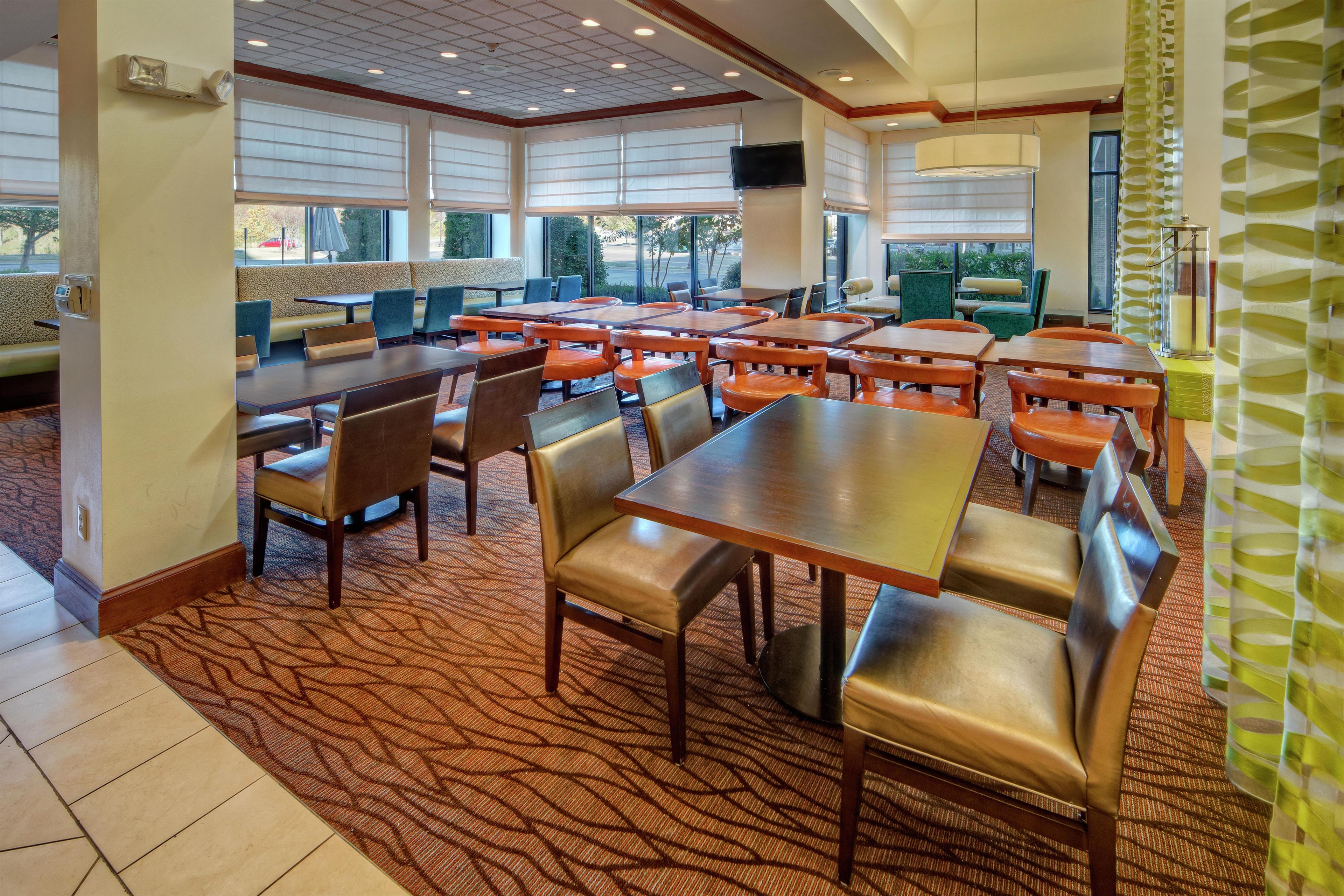 A restaurant with multiple tables and booths, carpeted flooring, and large windows providing views of the outdoors.