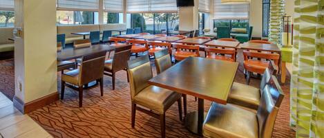 A restaurant with multiple tables and booths, carpeted flooring, and large windows providing views of the outdoors.