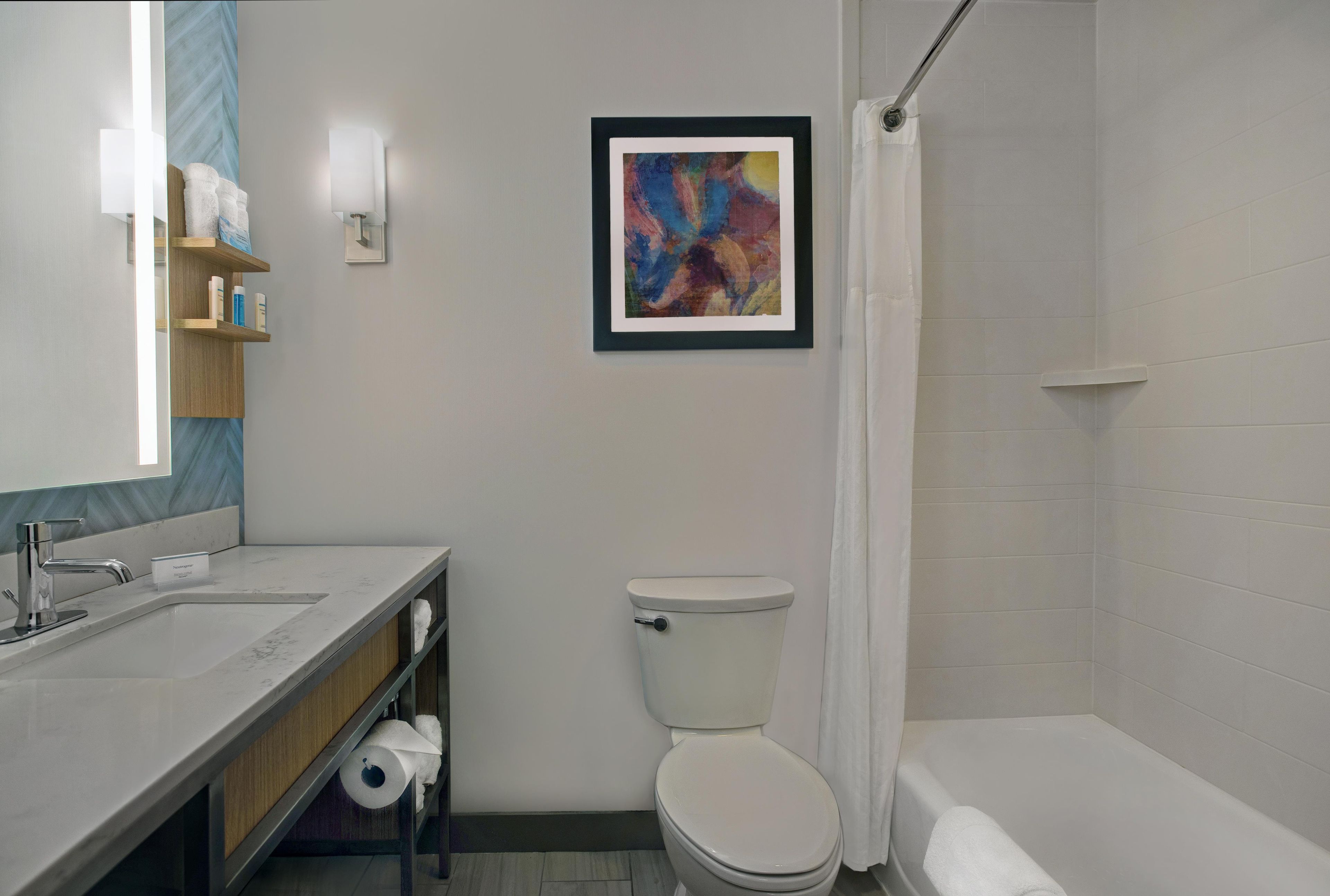 A bathroom with a toilet, a sink, a shower, and a framed abstract painting on the wall.