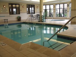 Una piscina interior con agua cristalina, un trampolín y un cartel de socorrista.