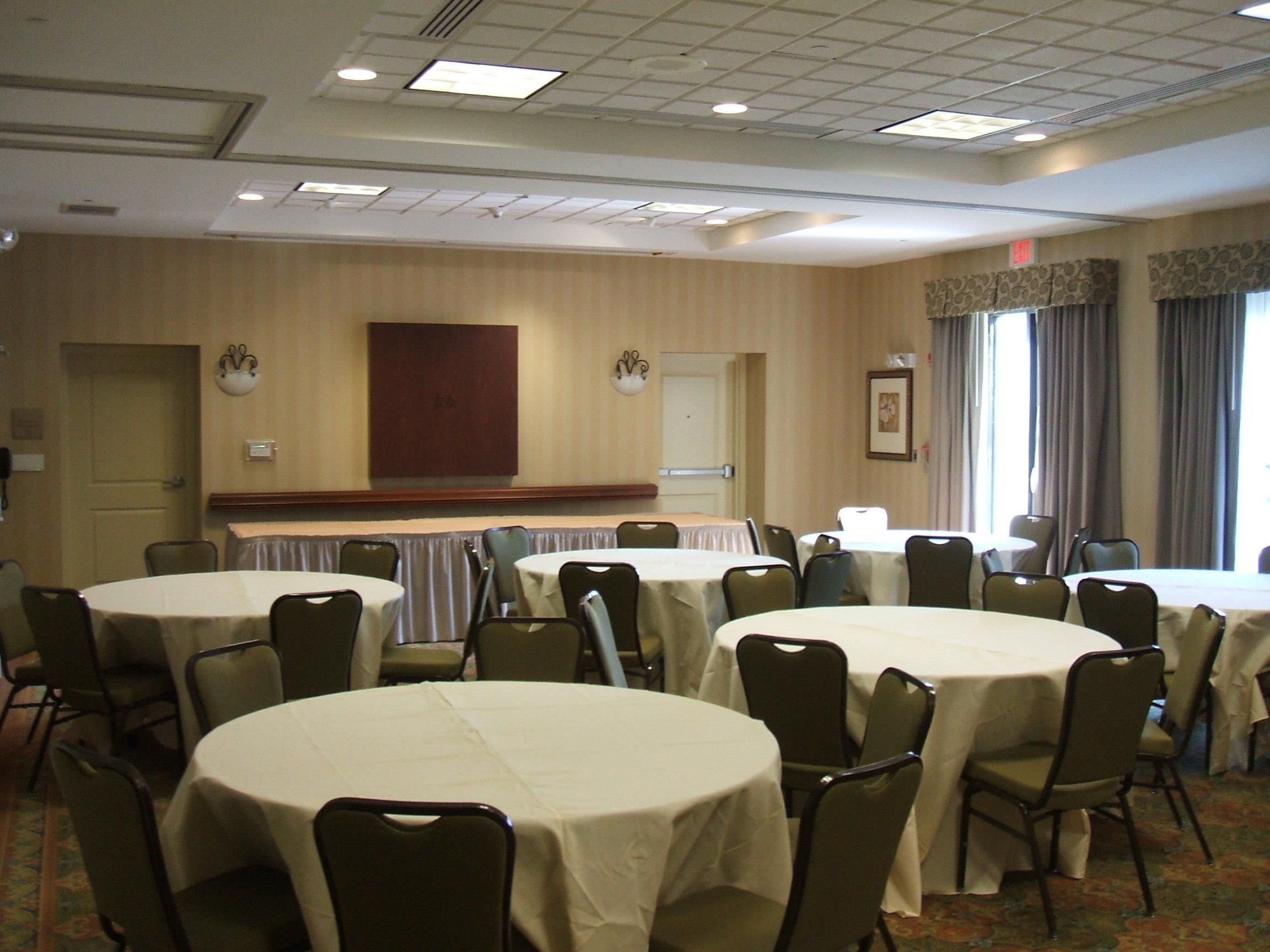 A conference room with multiple round tables and chairs, a wooden door, and a window with curtains.