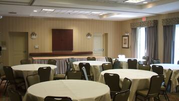 A conference room with multiple round tables and chairs, a wooden door, and a window with curtains.