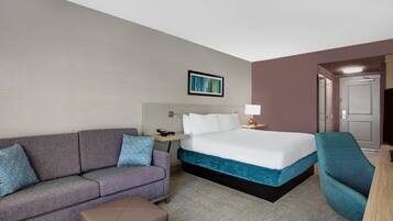A hotel room with a bed, a sofa, a chair, a desk, and a wall-mounted lamp.