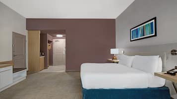 A hotel room with a bed, bedside table, lamp, and a painting on the wall.
