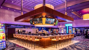 Un bar de casino con varias máquinas tragamonedas, una zona de bar central con taburetes y una alfombra estampada.