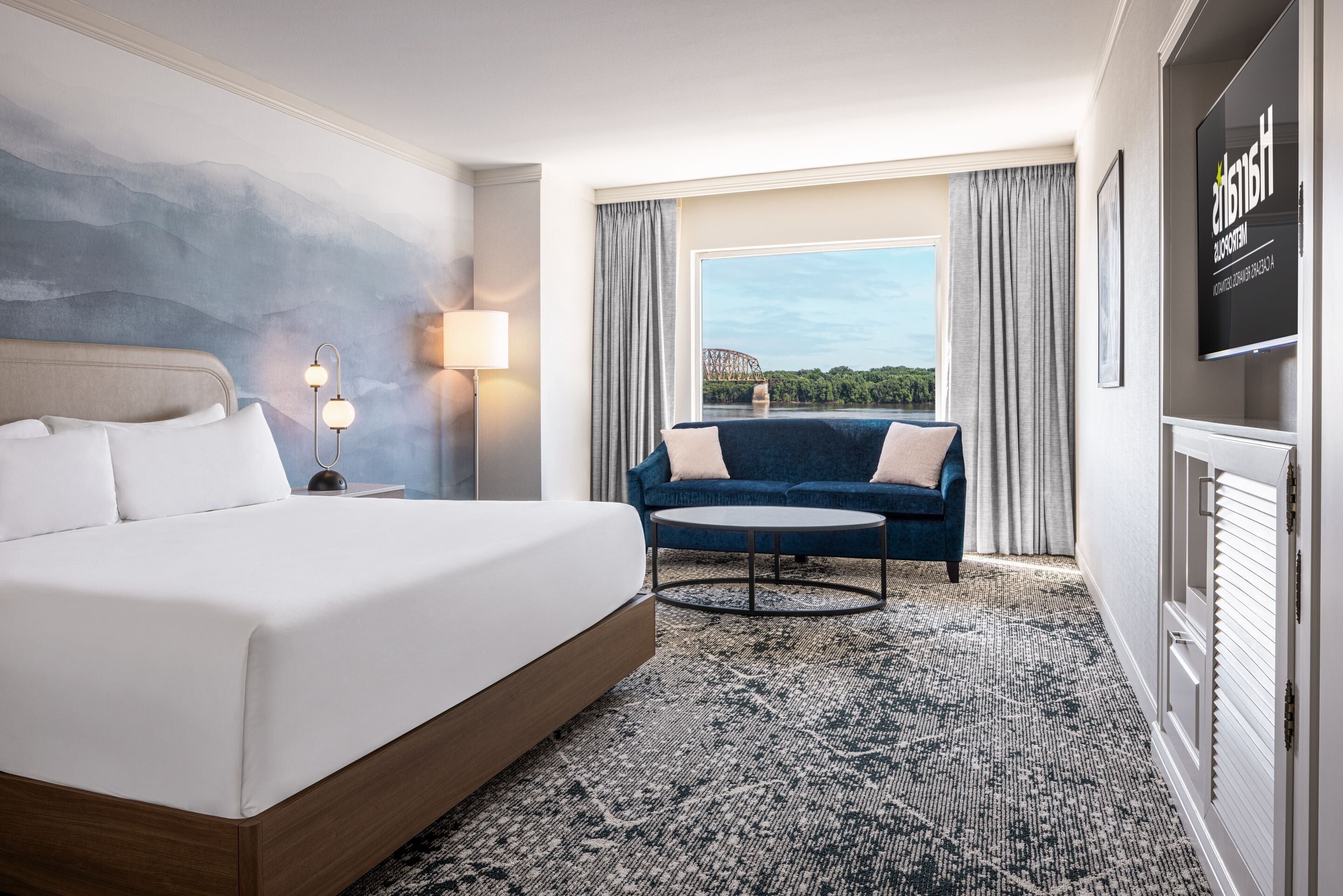 A hotel room with a large bed, a sofa, a small round table, and a TV on the wall.