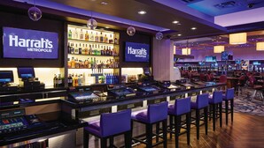 Zona de bar del casino Harrah's Metropolis con varias mesas de juego, una estantería repleta de licores y taburetes de bar.