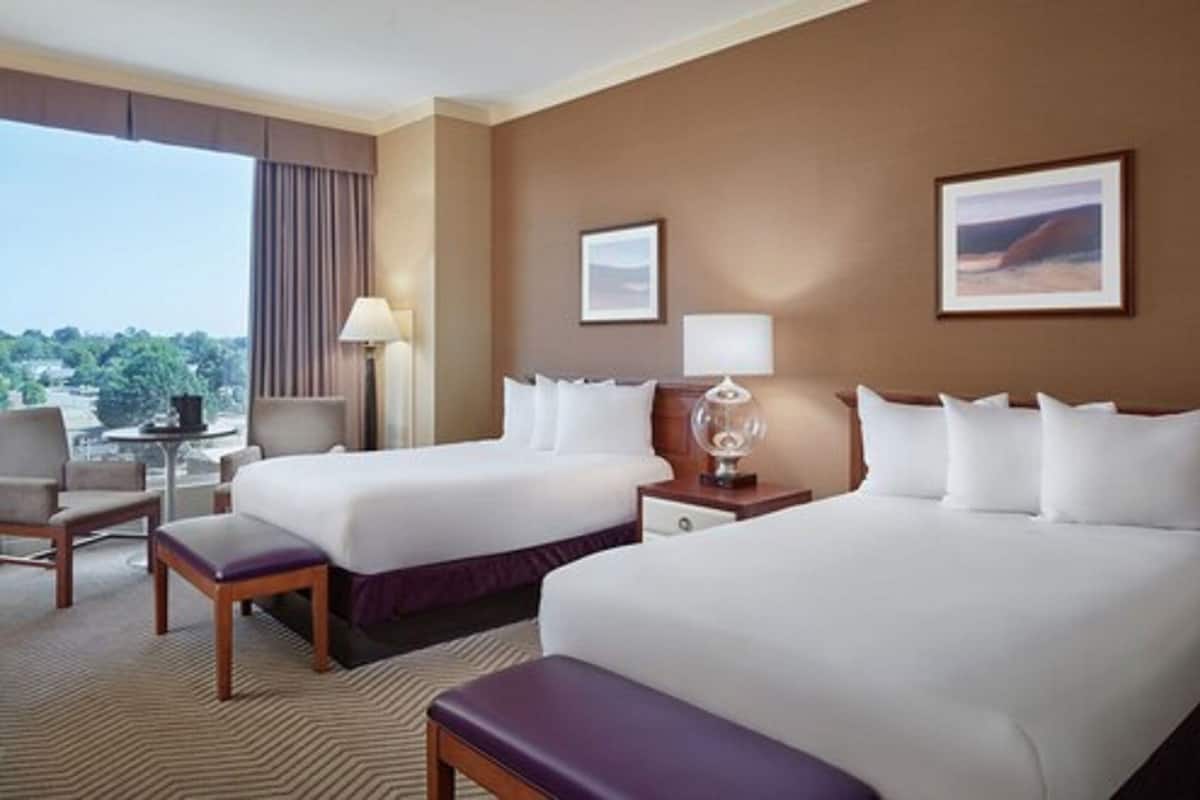 A hotel room with two beds, a chair, a table, and a lamp.